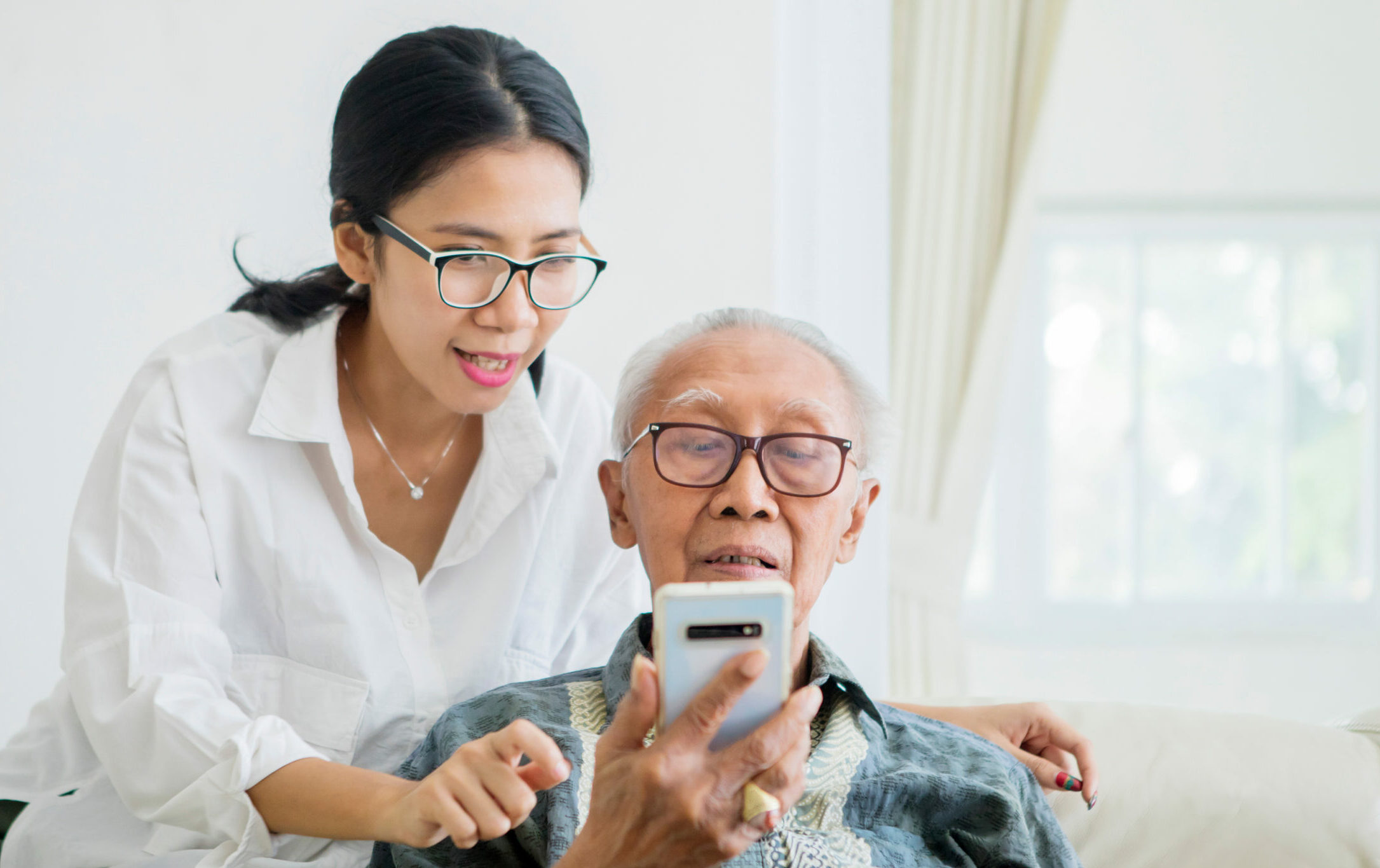 Young woman helping his father to using a mobile phone while sitting at home
